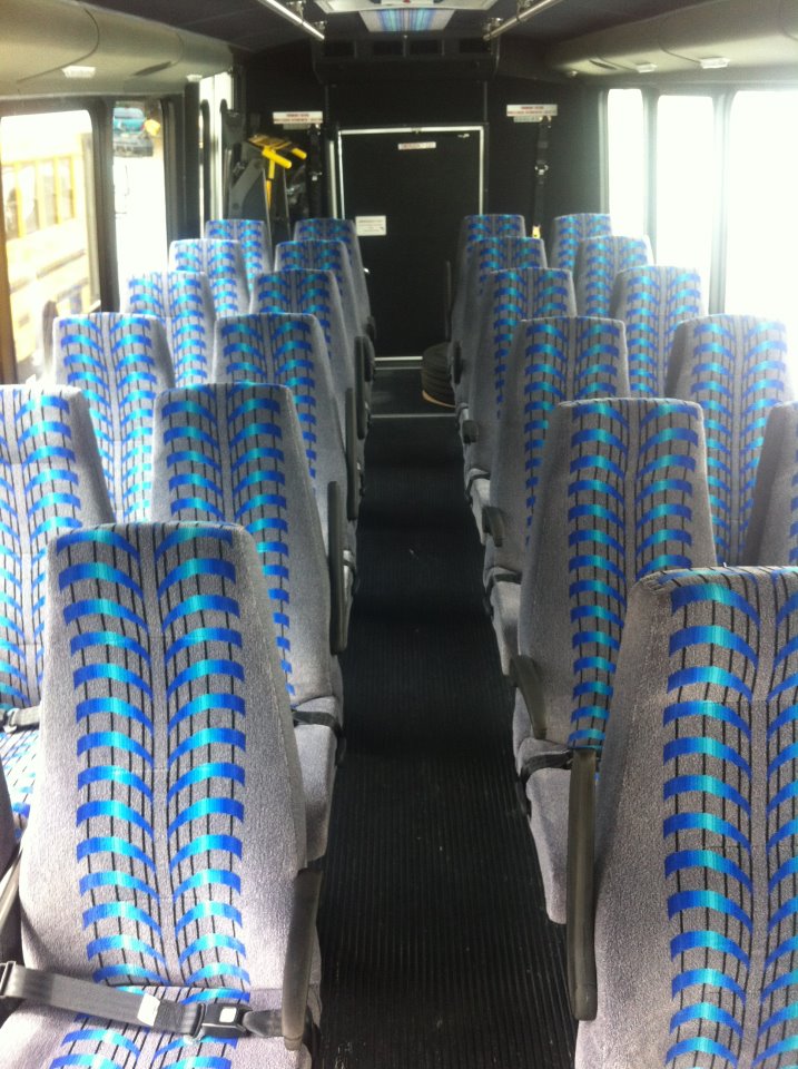 Inside of touring bus shiowing gray and blue seats with seatbelts.